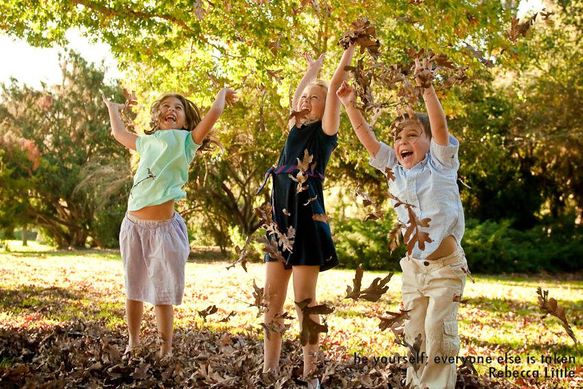 photograph of three children jumping in the leaves