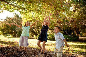 photograph of three children playing in the fall leaves