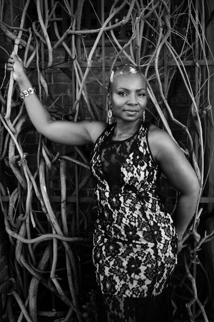 Isn't this a strong black and white portrait of Jo-Ann? She posed for this photos during a Day of Beauty put on by the Foundation for Living Beauty in downtown Pasadena. This black and white image shows her standing up in front of a large bare vine. The vine wraps around the metal fence and makes a fabulous backdrop.  She's wearing a black dress with flower cutouts. The is a black tulle inset over her cleavage. One arm angles up and grabs the vine and the other arm is down with her hand resting behind her back. Her arms are strong and muscled. Living Beauty is a nonprofit in Pasadena that helps women living with cancer. Rebecca Little Photography Pasadena, CA for creative headshots in Los Angeles.
