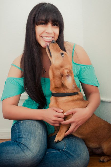 This is a lifestyle headshot of Carmel Mims, owner of Pet Porter Pals. Her business specializes in providing pet care assistance to seniors in order to ensure proper health of their pets. Carmel is more than a dog walker, though she takes excellent care of your fur babies and also includes dog walking in her services. She wanted fun lifestyle headshots for her Pasadena dog walking business and we created these in my photos studio on Green Street in Pasadena. She’s wearing a fun sea-green off-the-shoulder top and is with her dog client Beefy. We wanted to show that dog walkers are fun and professional, and she will take good care of your pets.  Rebecca Little Photography placed her in front of her big window and bathed her in beautiful natural light. Beefy is giving her a big kiss and Carmel is smiling and loving it!