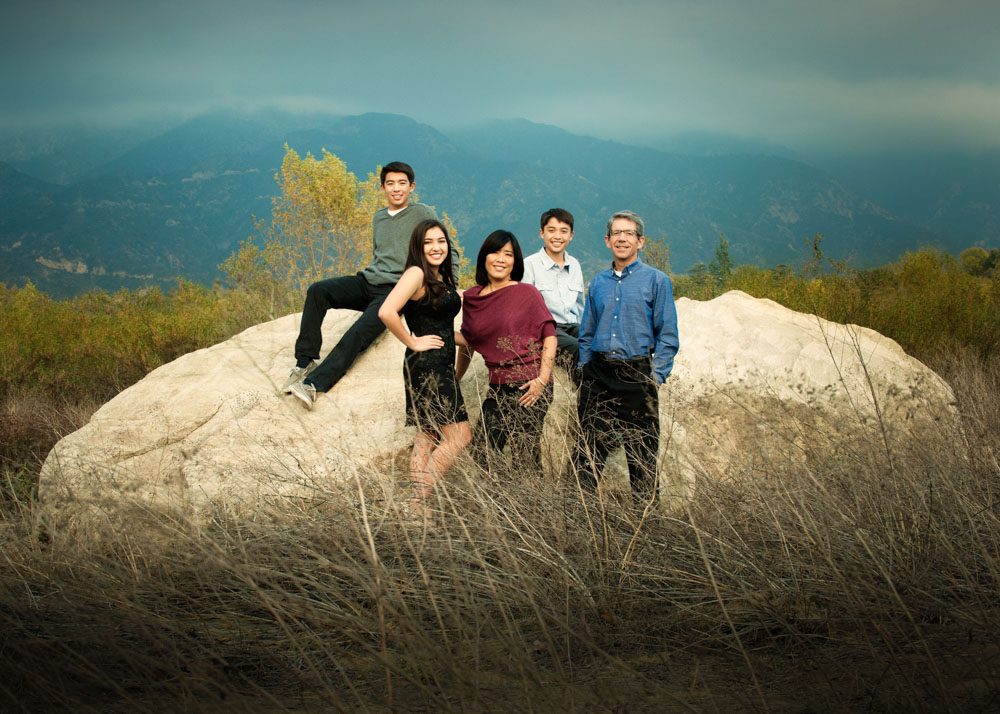 A family of five at a La Canada outdoor location for holiday photos. They are standing in front of a large white boulder.