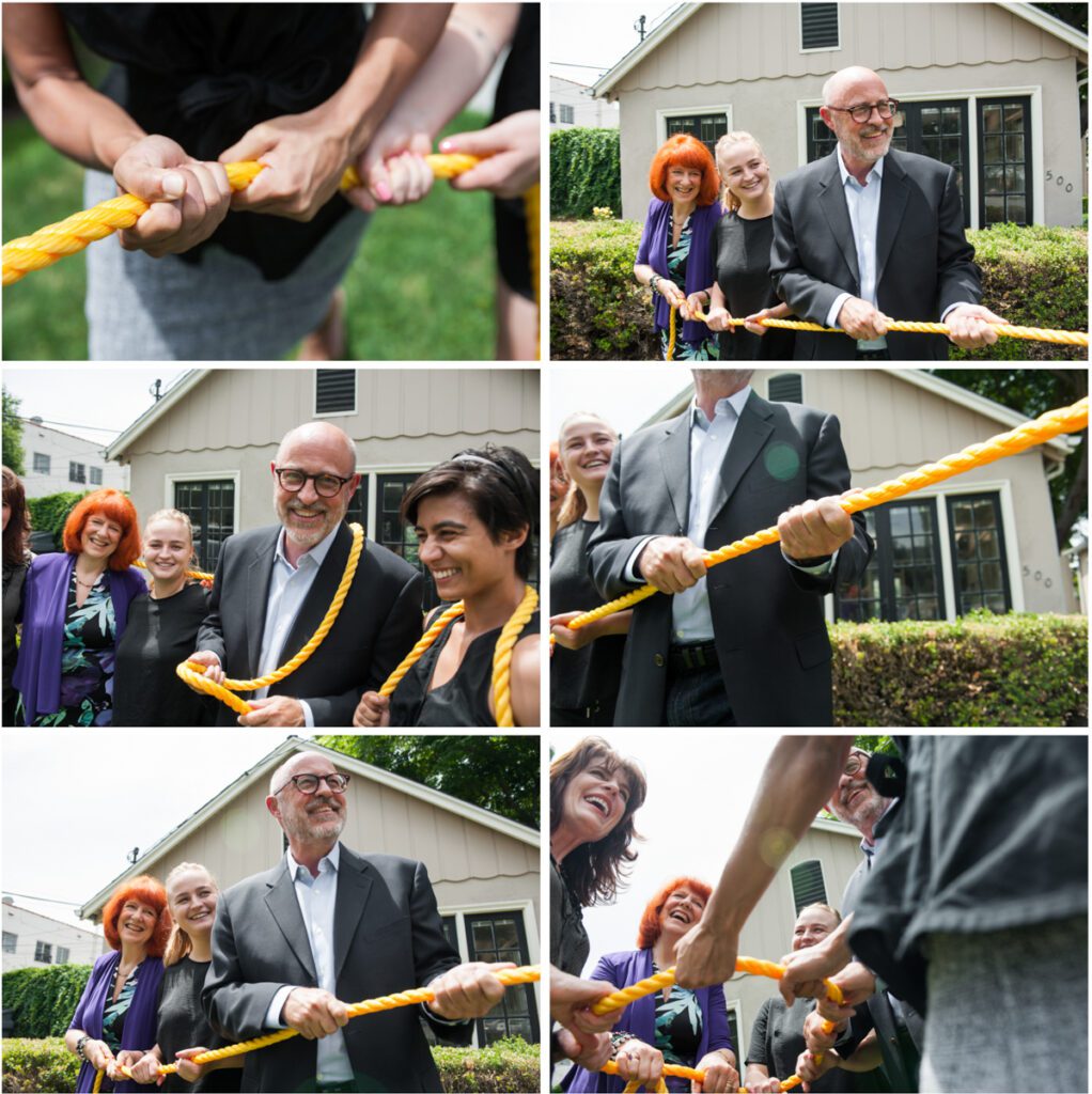 This is a collage of six images showing people playing tug of war. It's a bright sunny day and they are outside standing in front of a white house that serves as the CEO's office. There is a man in his late 50's wearing a dark suit and button down shirt. He had black glasses and a friendly demeanor. There is a redheaded woman in her early 60's with a purple cardigan. Beside her is a blond woman in her 20's wearing a black t-shirt. There's another woman in her 20's wearing a sleeveless black shirt and a woman in her 40's with her medium-length hair cut stylishly. They are all smiling, laughing, and having a good time. The rope is thick and bright yellow, They have it wrapped around their hands and are pulling in opposite directions. The GenXers are on one side and the Baby Boomers are on the other. This branding photo illustrates that different generations are often at odds and working against each other. Image created by rebecca Little Photography Pasadena, CA.