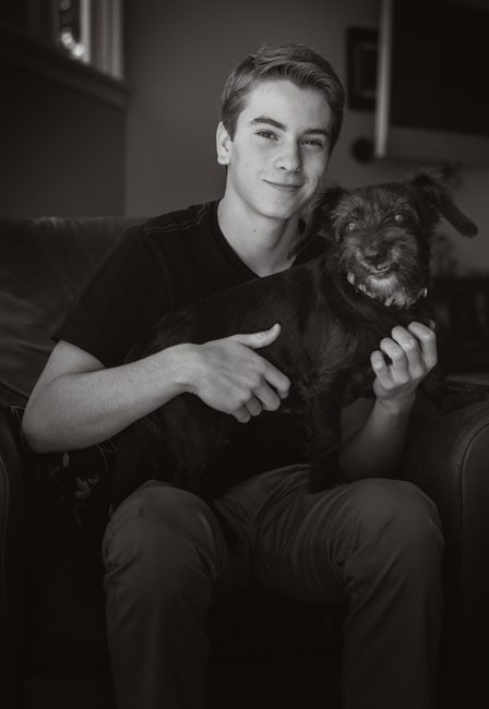 This is a black and white senior portrait of Pasadena high school senior Aaron. I love creating senior portraits! We created this photo at 
this high school senior's home. He wanted to pose with his dog Licorice. He's sitting in a chair in front of a large window holding his dog on his pap. Aaron is well lit, but we kept some shadows for dramatic contrast. He's wearing jeans and a black t-shirt, and Licorice the dog is black. He's a small dog and easily fits on Aaron's lap.It's important to create a variety of high school senior portraits and take some in the studio and some outdoors. Parents usually have their own ideas about the kind of senior portraits they want for their high schooler and I take everyone's opinion into account. I suggest you bring a suit and tie, a sweater with some texture, jeans and a t-shirt, a button-down shirt, and a shirt with a pop of color. This way I can photograph a nice variety. You may even be able to use one of the photos in the high school yearbook, but you have to check with your school. These senior portraits are perfect for family gifts and graduation announcements. This photo was taken by Rebecca Little Photography in Pasadena, CA.