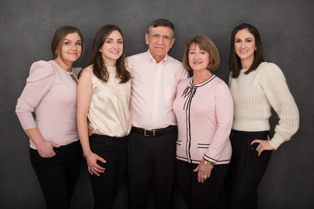 A family of five posing for family photos in my Pasadena studio. They are standing in font of a charcoal hand-painted canvas backdrop. They're wearing black pants and. sweaters, blouses, and shirt in shades of pink and ivory. This is a stunning example of how to color coordinate your outfits for family photos. Image created by Rebecca Little Photography Pasadena, CA.