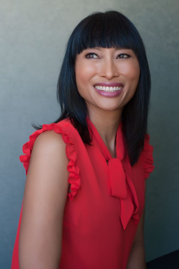 This is an updated headshot for Anna’s job search. She’s wearing a vivid red-orange sleeveless blouse with a tie collar. She is sitting. Her face is facing to the left and she’s not looking at the camera. Non-camera aware images are popular and have a casual, relaxed feel when the subject is laughing, as Anna is. Her black hair is to her shoulders and she has bangs cut straight across her forehead. She has straight white teeth and dark eyes. The image portrays confidence, happiness, and sophistication and was created by Rebecca Little Photography in Pasadena, CA.